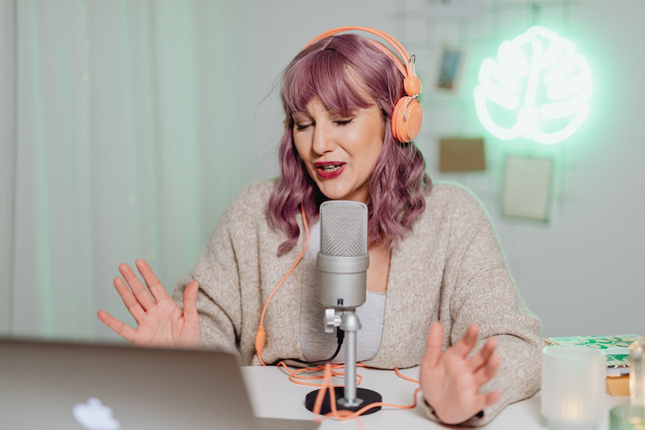 Woman podcasting indoors with headphones and microphone, engaging in recording or live stream.