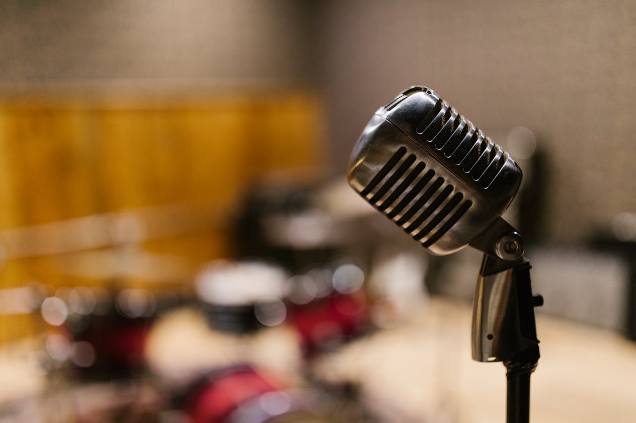 Close-up of a vintage microphone in a music studio with blurred drum set in the background.